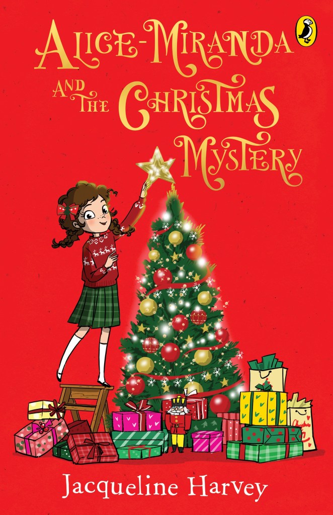 A red book with gold writing that reads Alice-Miranda and the Christmas Mystery by Jacqueline Harvey. A brown-haired girl in a red jumper and green skirt is standing on a stool by a Christmas tree with shiny lights and red and gold baubles on it. She is smiling as she puts a star on the top, and there are colourful presents under the tree. The gold is shiny and sparkly on the cover. 