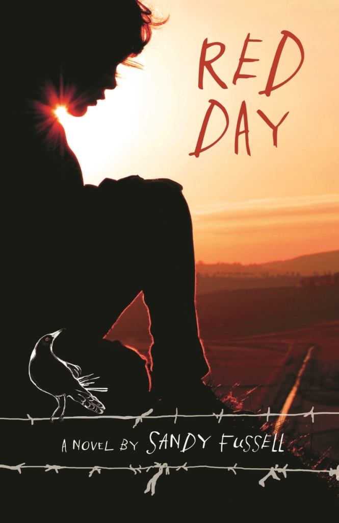 A boy or girl  behind barbed wire against the country and a sunset. Text says Red Day: A Novel by Sandy Fussell