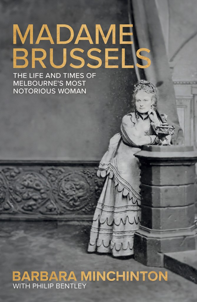 A black and white photo of Madame Brussels leaning against a wall. Madame Brussels is in gold text and the subtitle is in white text.