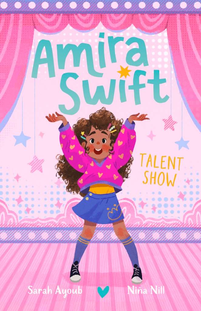 Amira Swift: Talent Show 

A brown girl with curly brown hair on a pink and purple stage with colourful stars behind her. She is wearing pink, yellow and purple clothes. The title text is around her and is in turquoise and yellow. 
